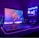 A gaming setup with a monitor displaying a colorful 'Republic of Gamers' logo, accompanied by a mechanical keyboard and a gaming mouse on a desk illuminated with RGB lighting. The computer tower is visible, featuring internal cooling fans lit with vibrant blue and purple LED lights.